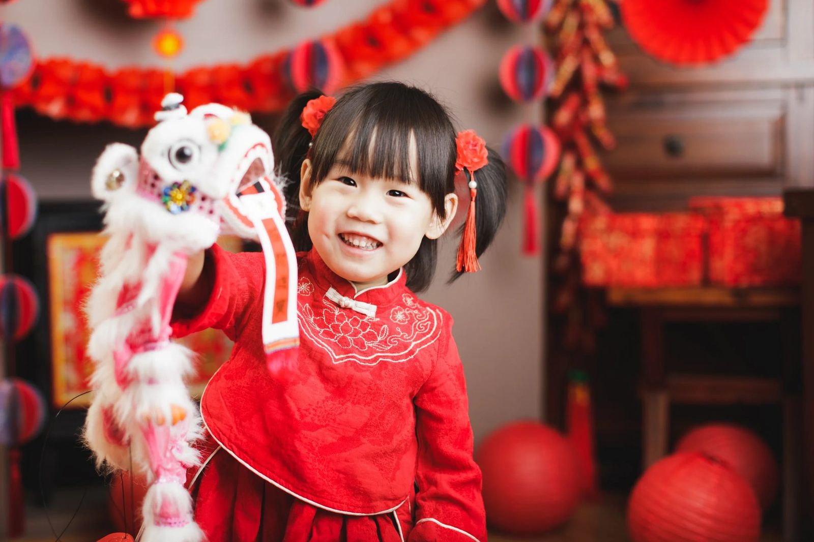 A young girl smiles while holding a lion dance puppet at a Lunar New Year celebration